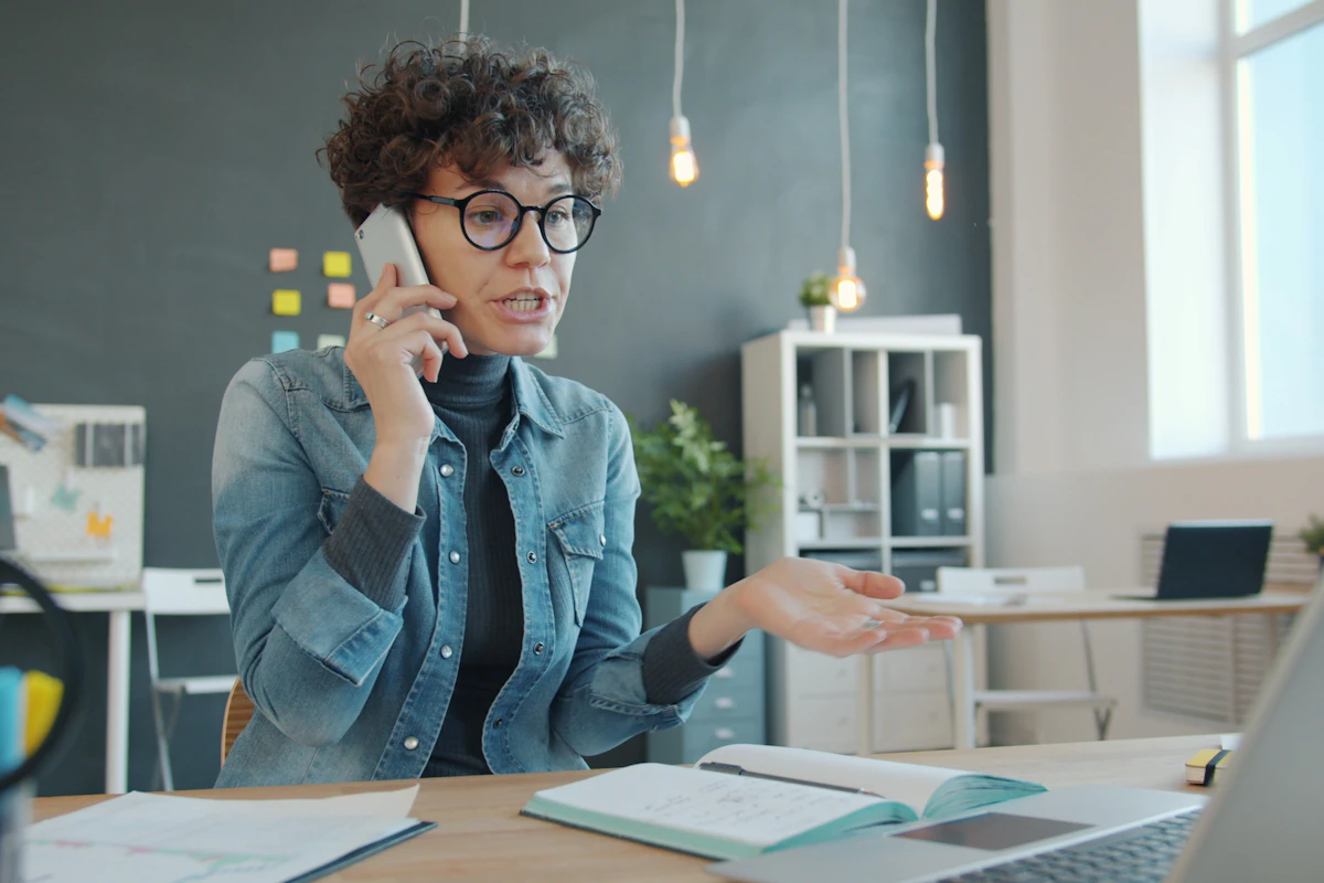 A woman taking a mobile phone call at her desk in a naturally lit office